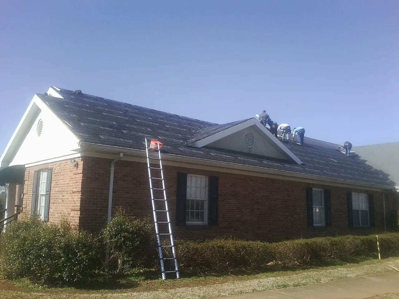 Crew tearing shingles off a brick ranch roof with a ladder set — Metal Roof Repair work by our crew in Mahaffey