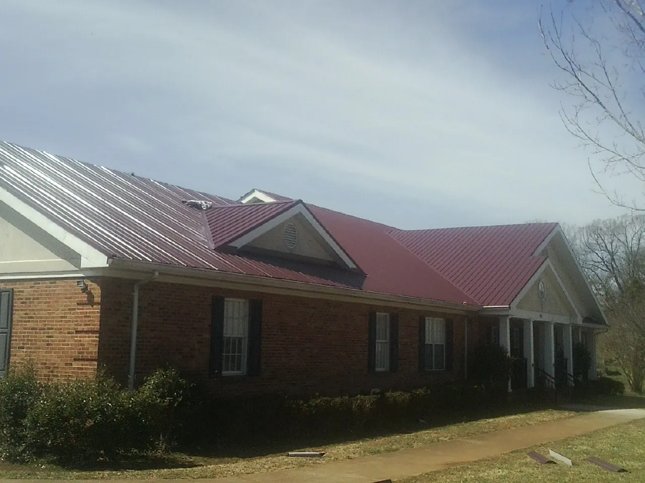 Red metal roof with gabled entries on a long brick building, from a Hail Damage Roof Repair job in Mahaffey