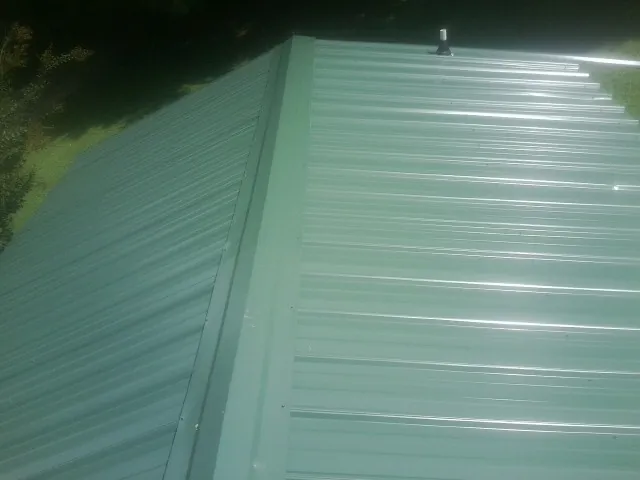 New green metal panels meeting at the ridge of a roof — Flat Roof Repair work by our crew in Mahaffey
