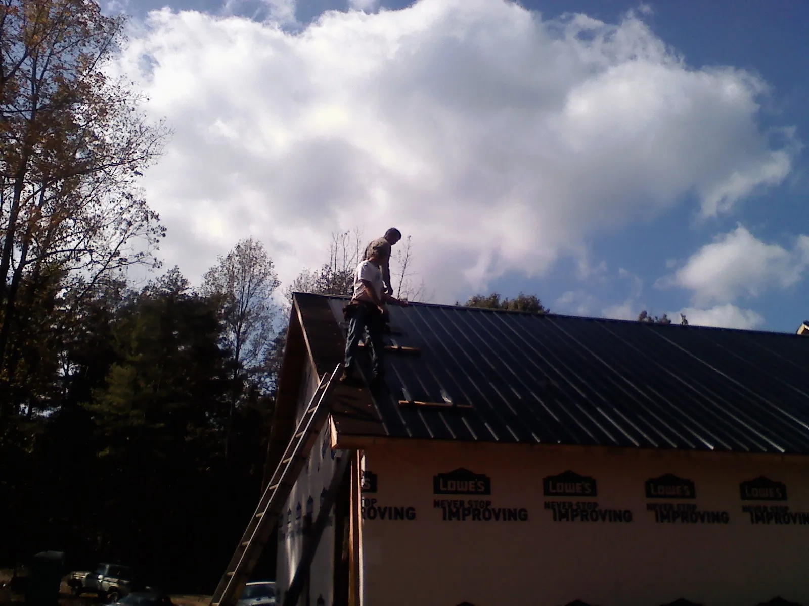 Roofer fastening dark metal panels high against a cloudy sky, from a Roof Inspection job in Mahaffey