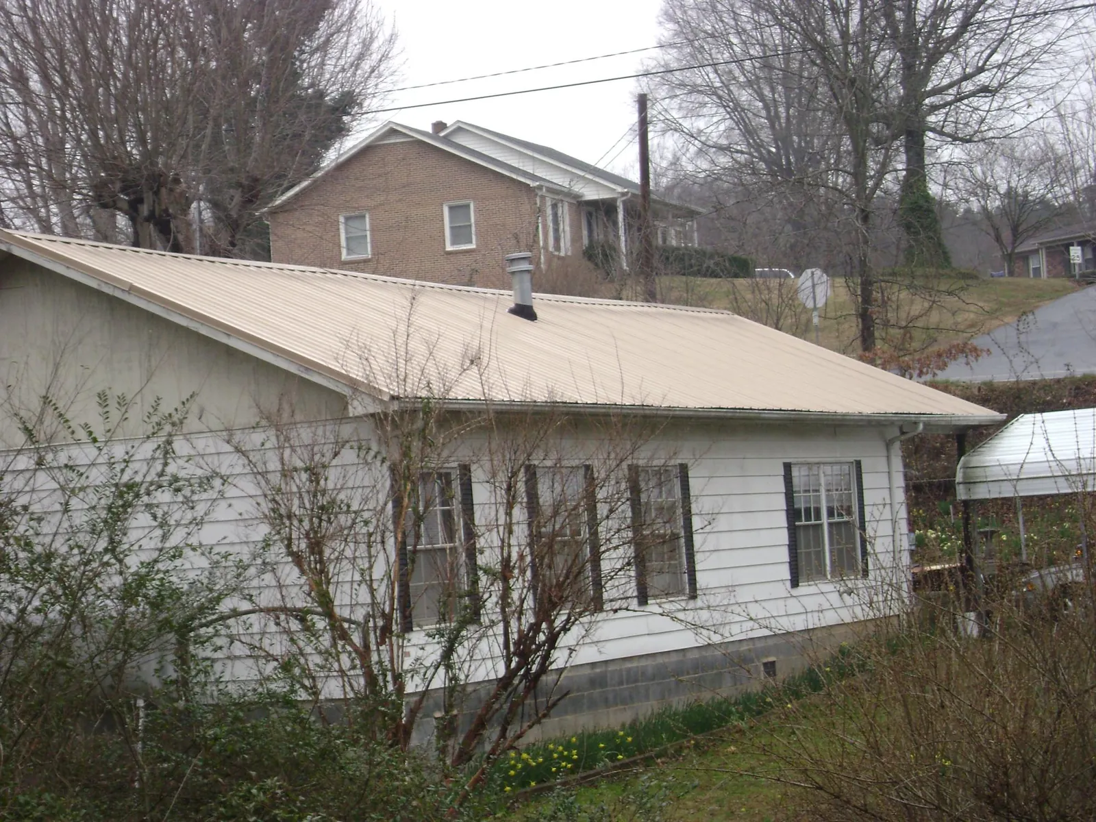 Tan metal roof on a white sided house set into a hillside — Commercial Roofing by Roofing Brothers in Mahaffey